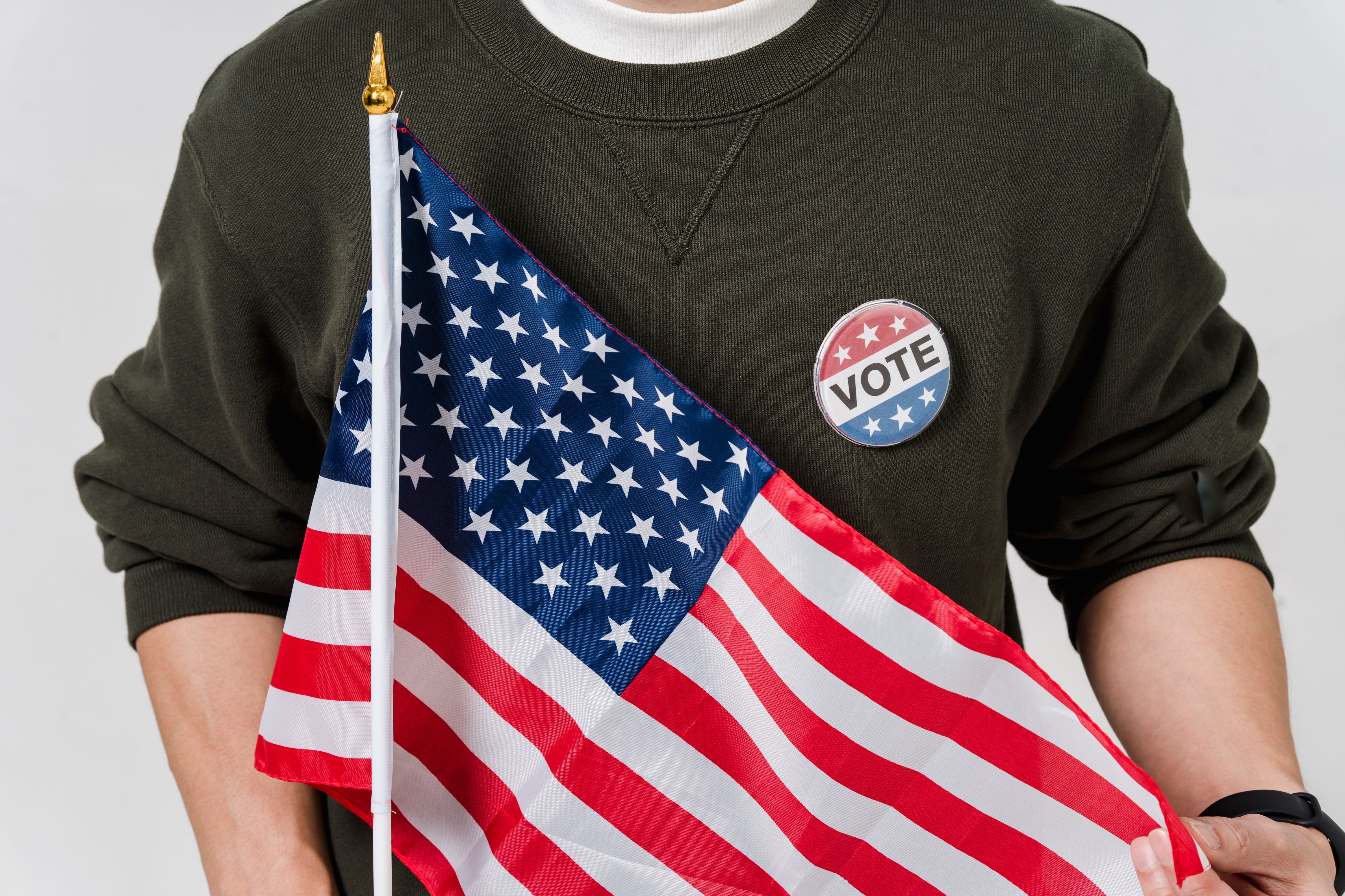 A person holding an American flag with a vote badge, symbolizing democracy