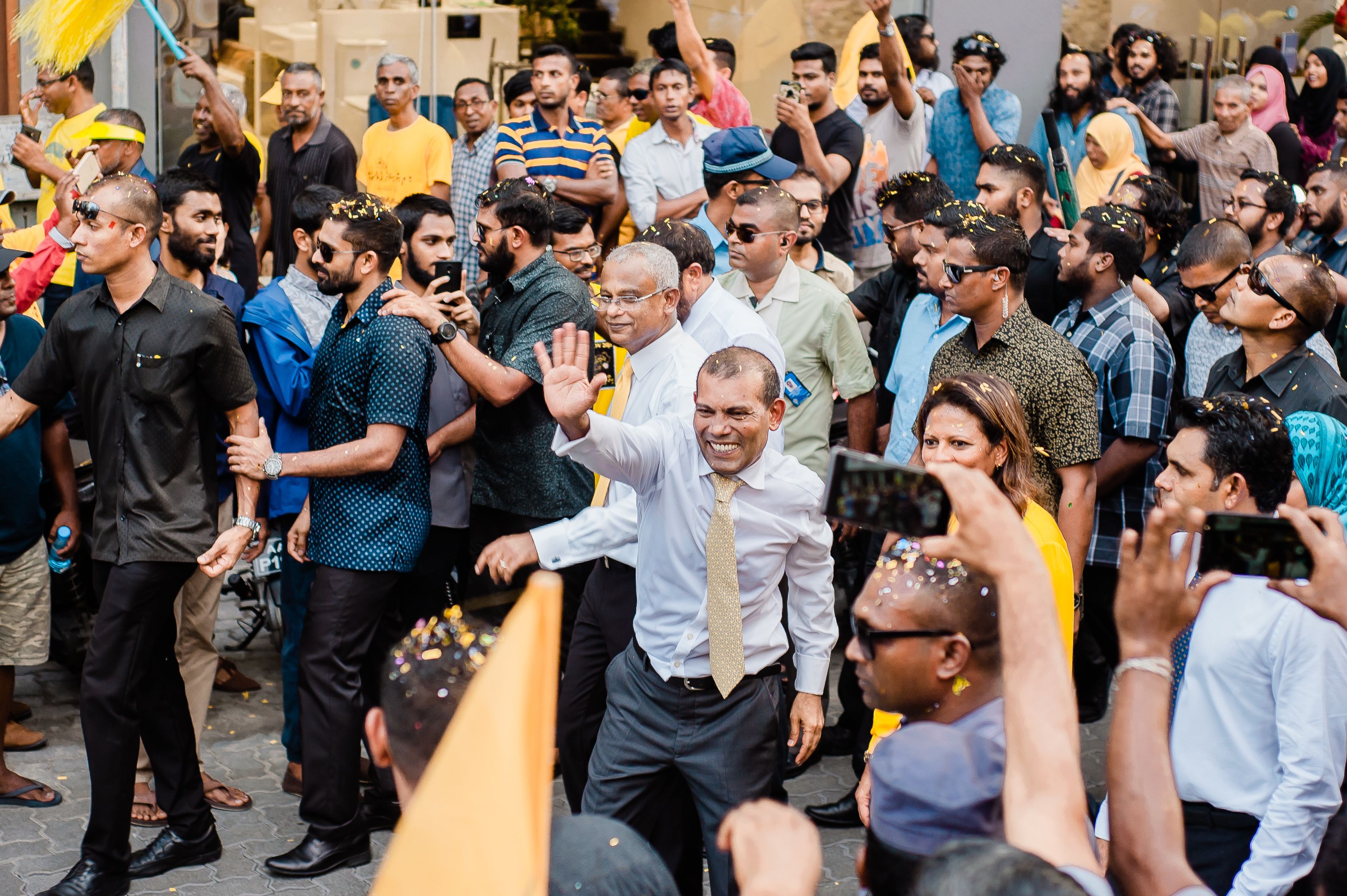 A politician waving to a crowd during a lively outdoor campaign rally