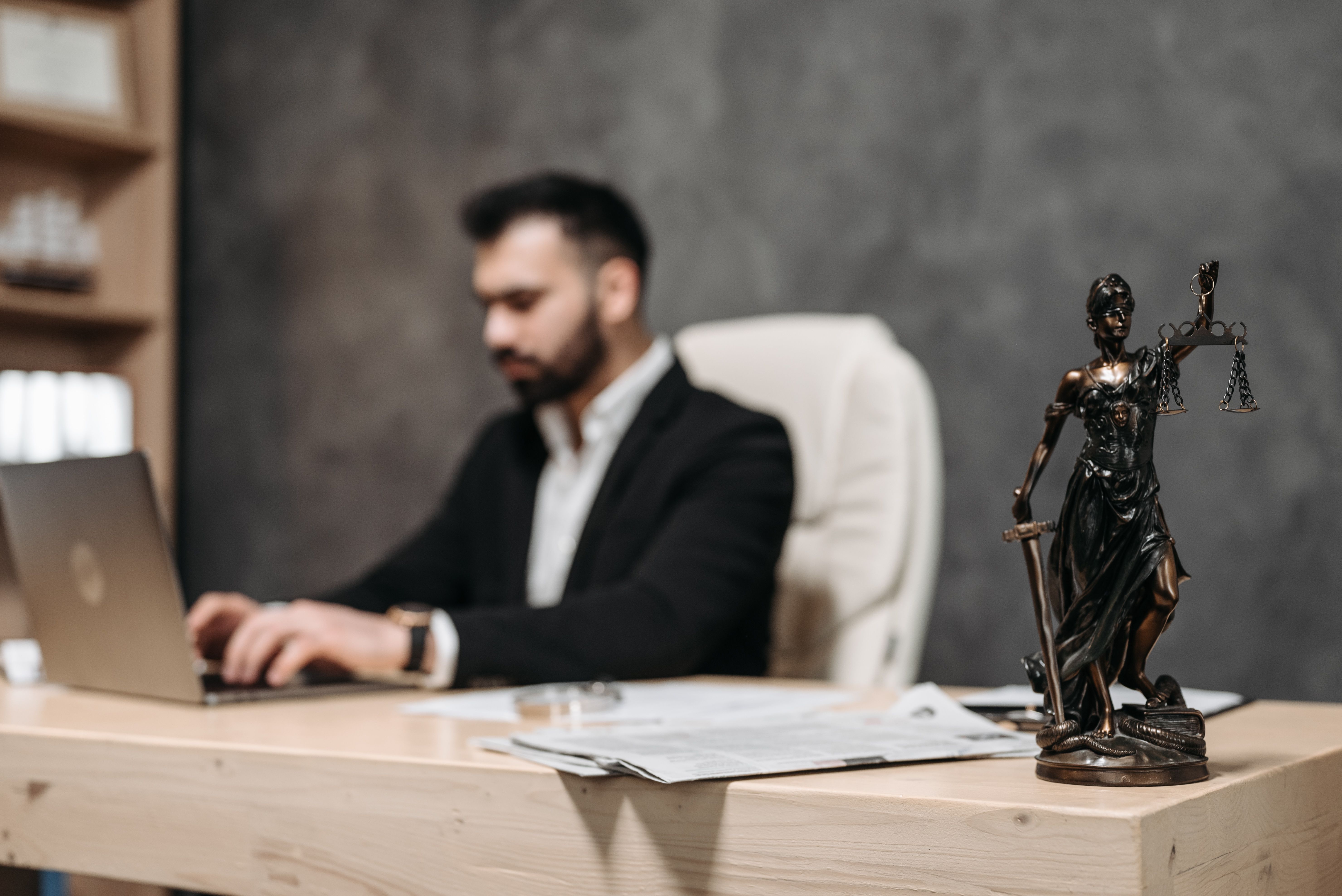 Lawyer working at a desk beside a Lady Justice statue in an office