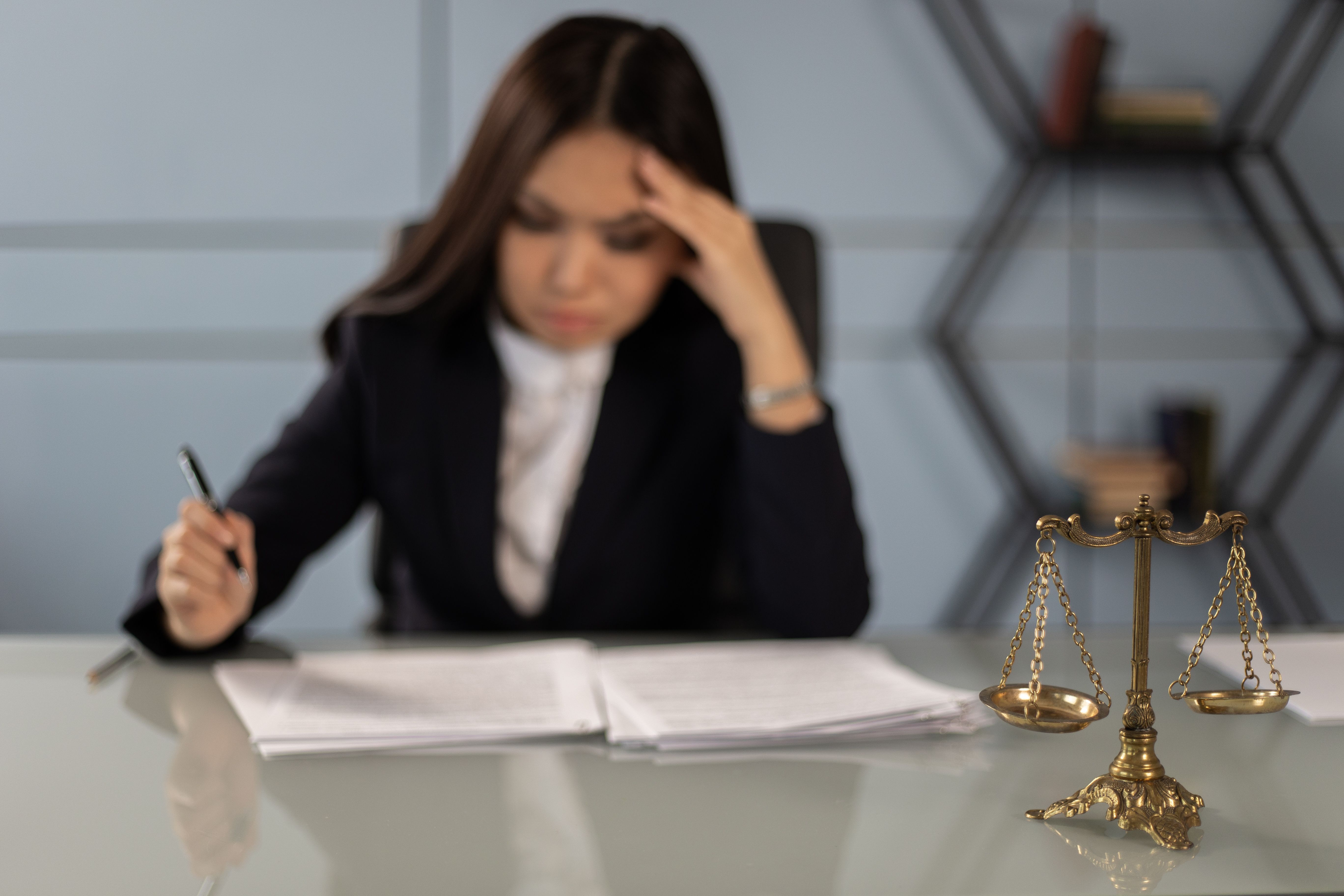 Fatigued lawyer reviewing legal documents with a justice scale nearby, illustrating the cost burden of litigation