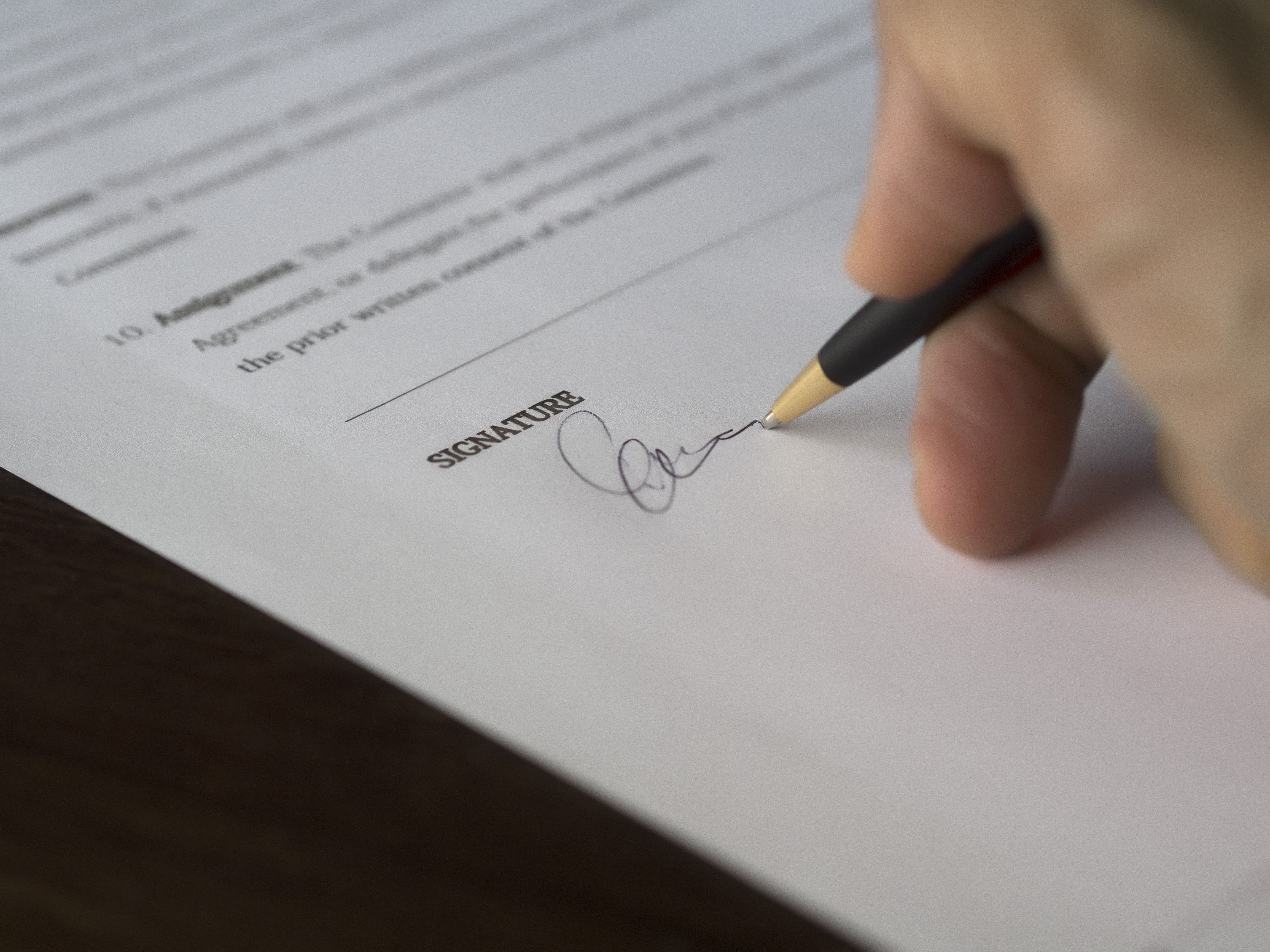 Hand signing a formal funding agreement with a pen on a wooden desk