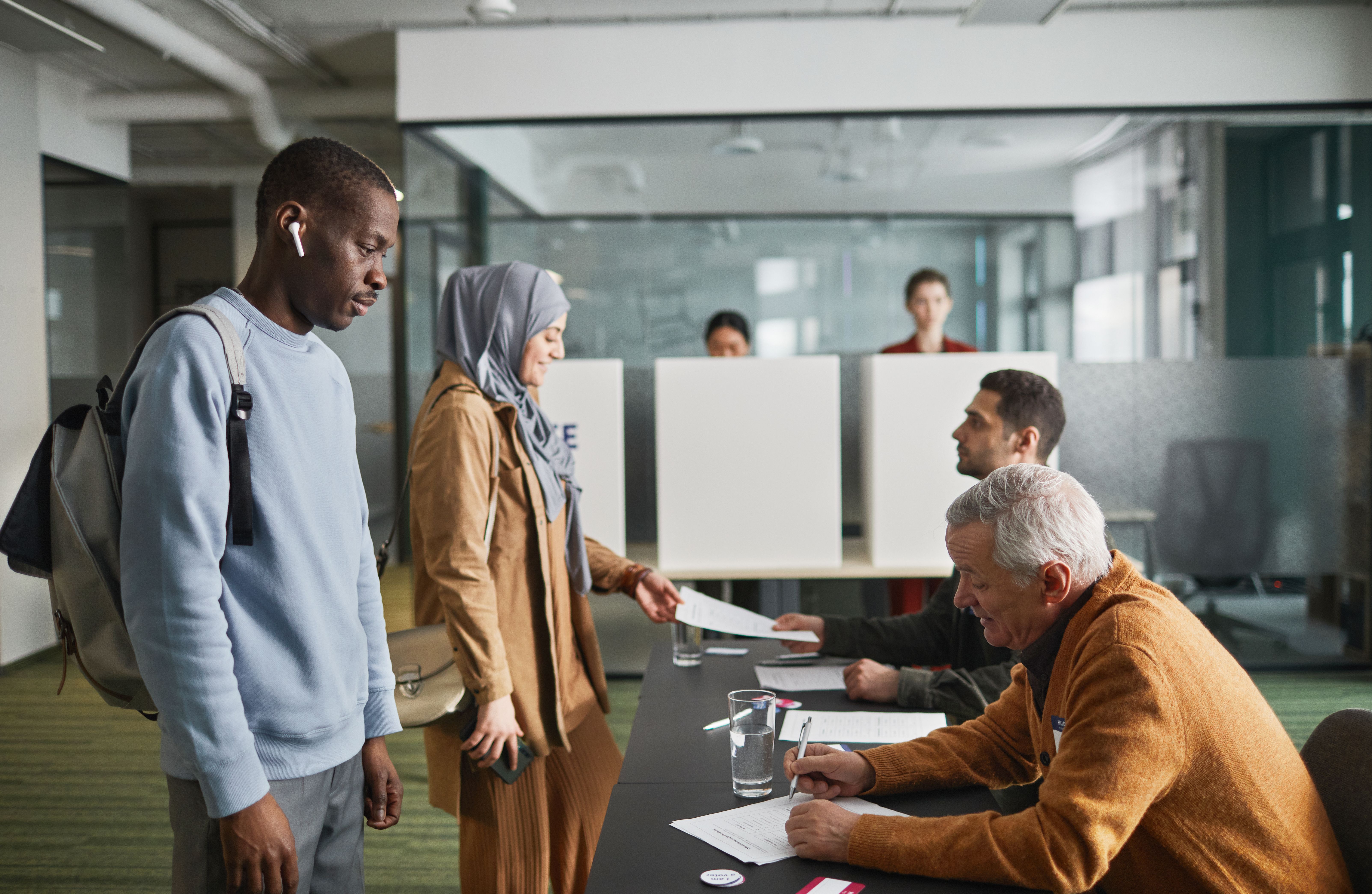 A diverse group of adults voting at an indoor polling station on election day